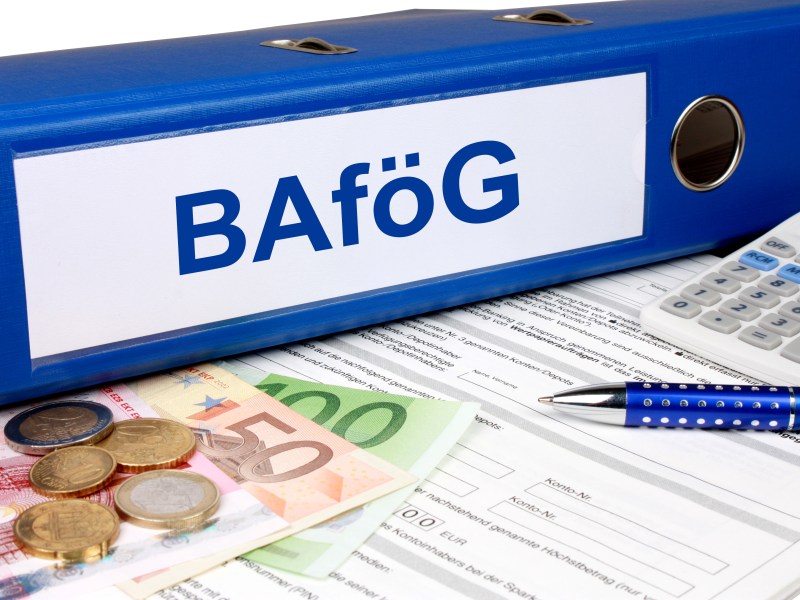 Auf einem Ordner mit der Aufschrift "BAföG" liegt auf einem Antrag. Daneben liegen Münzen und Geldscheine.