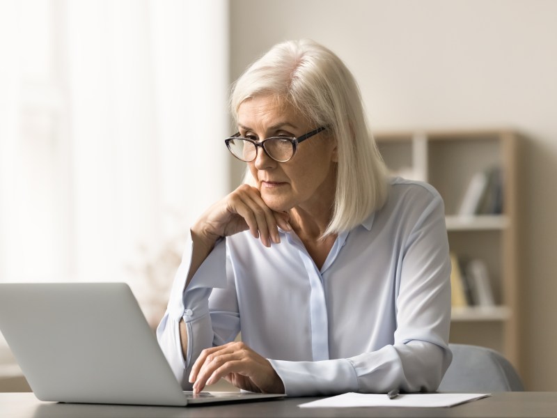 Eine ältere Dame sitzt vor dem Laptop und arbeitet.
