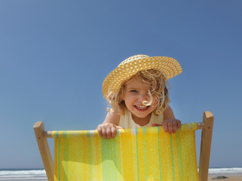 Kind mit Sonnenhut auf Strandliege in der Sonne