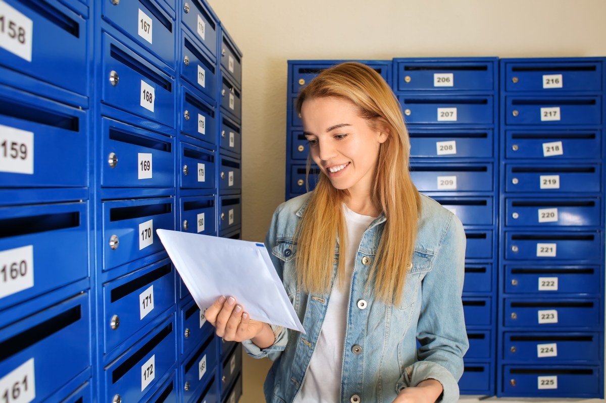 Eine junge Frau holt einen Brief aus ihrem blauen Briefkasten.