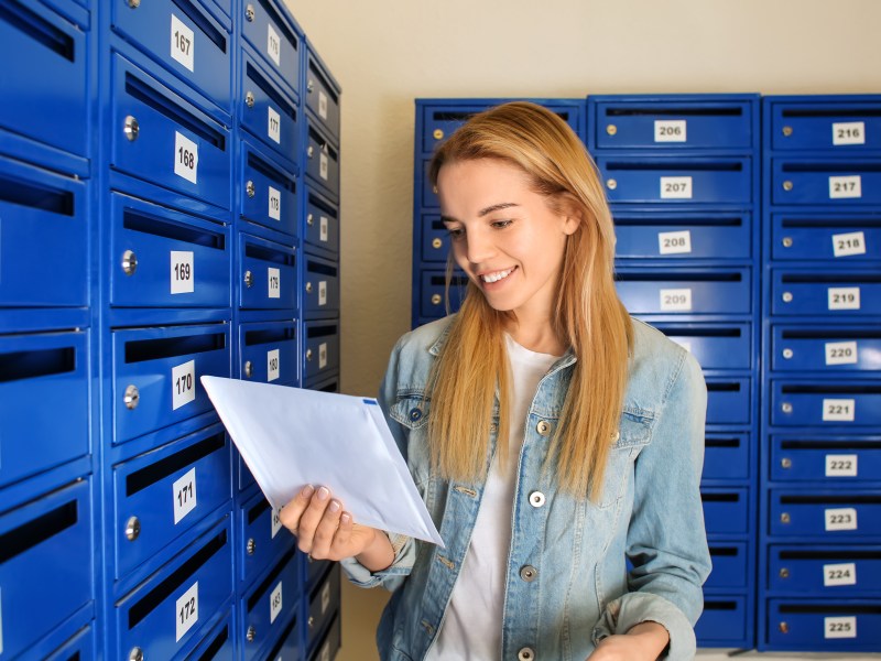 Eine junge Frau holt einen Brief aus ihrem blauen Briefkasten.
