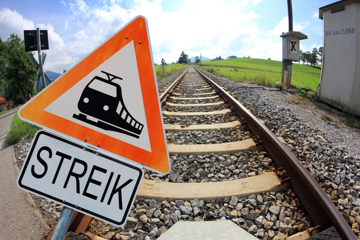 Auf einem Warnschild ist ein Zug abgebildet. Darunter steht das Wort "Streik". Dahinter verlaufen Gleisen.