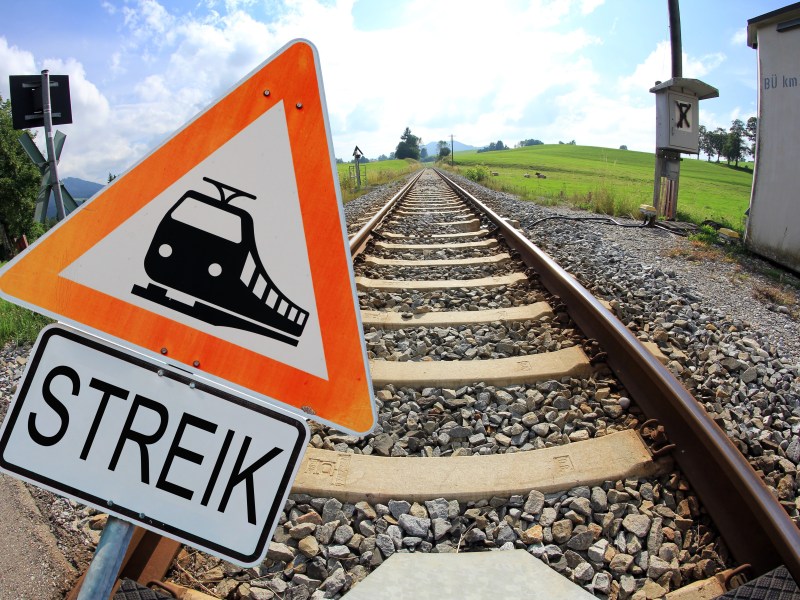 Auf einem Warnschild ist ein Zug abgebildet. Darunter steht das Wort "Streik". Dahinter verlaufen Gleisen.