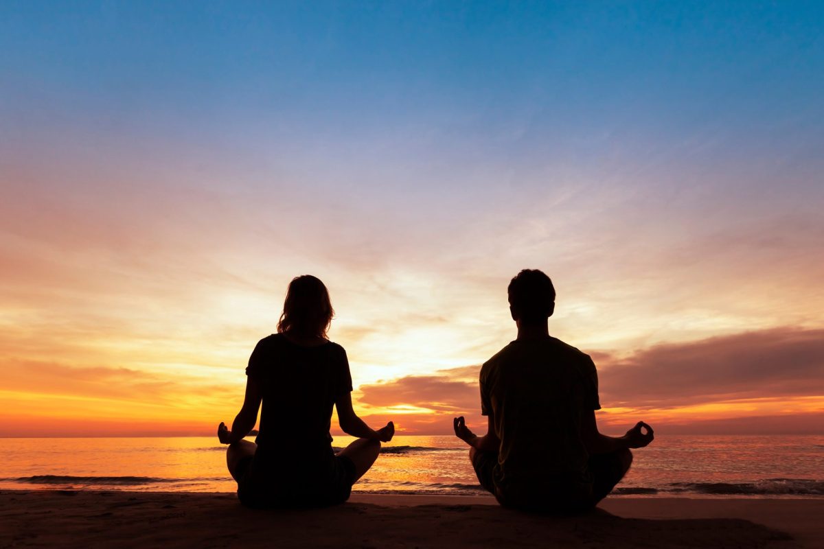 Zwei Menschen meditieren bei Sonnenuntergang mit Blick auf das Meer.