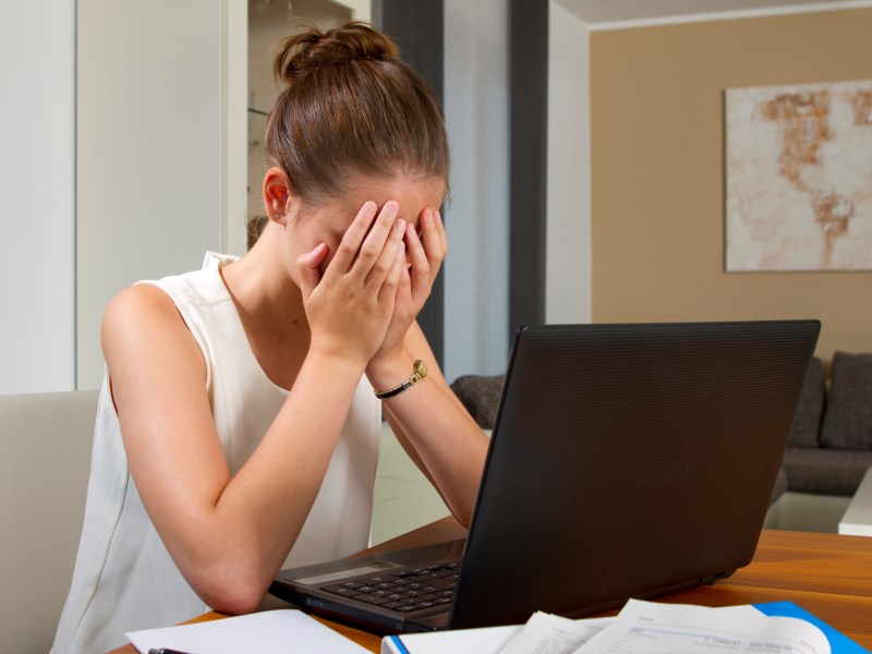 Eine Frau sitzt vor ihrem Laptop und hält die Hände vor ihre Augen.