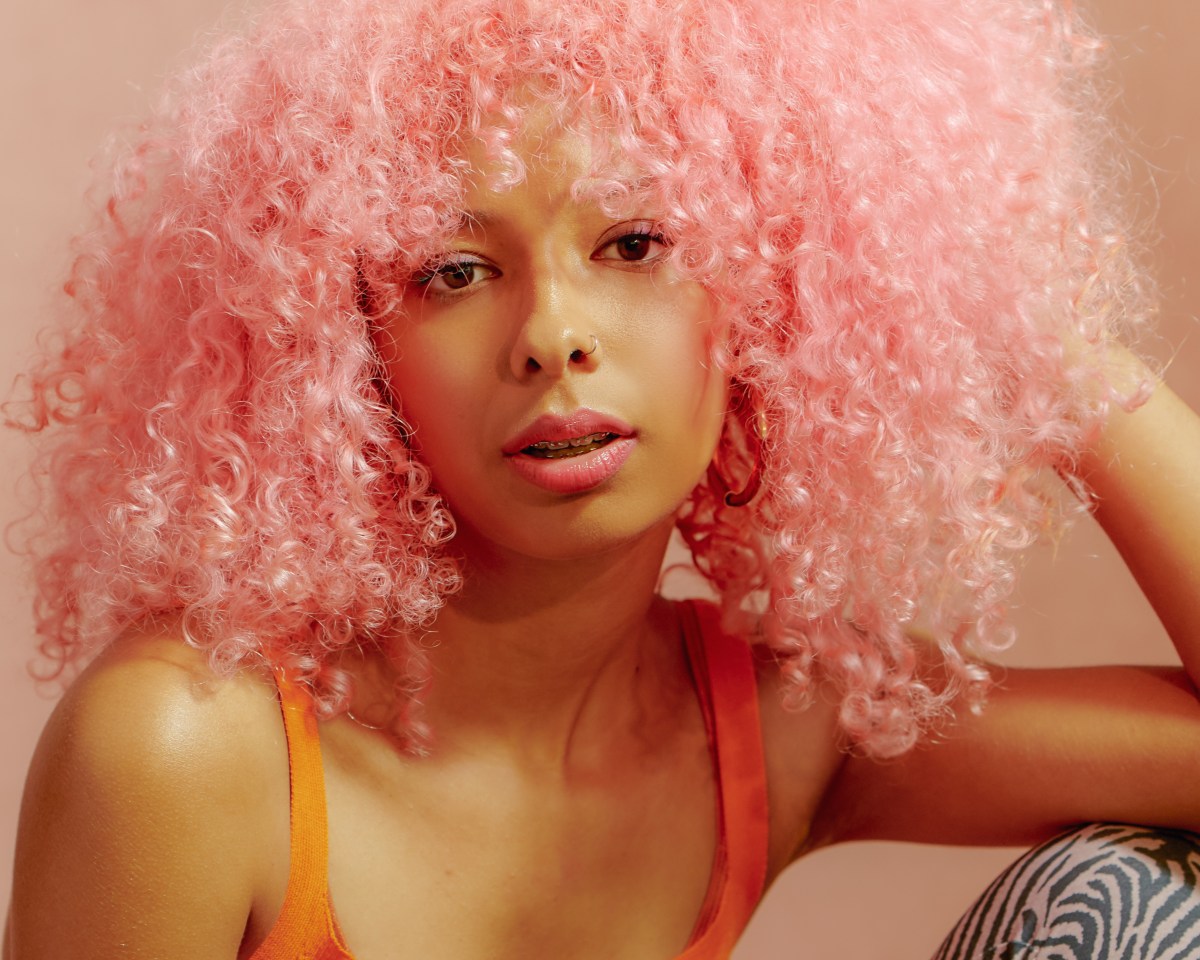 Frau mit rosanem Afro zeigt, welche Haarfärbetrends 2024 in sind!