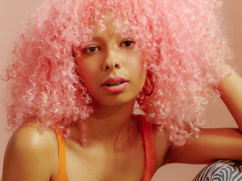 Frau mit rosanem Afro zeigt, welche Haarfärbetrends 2024 in sind!