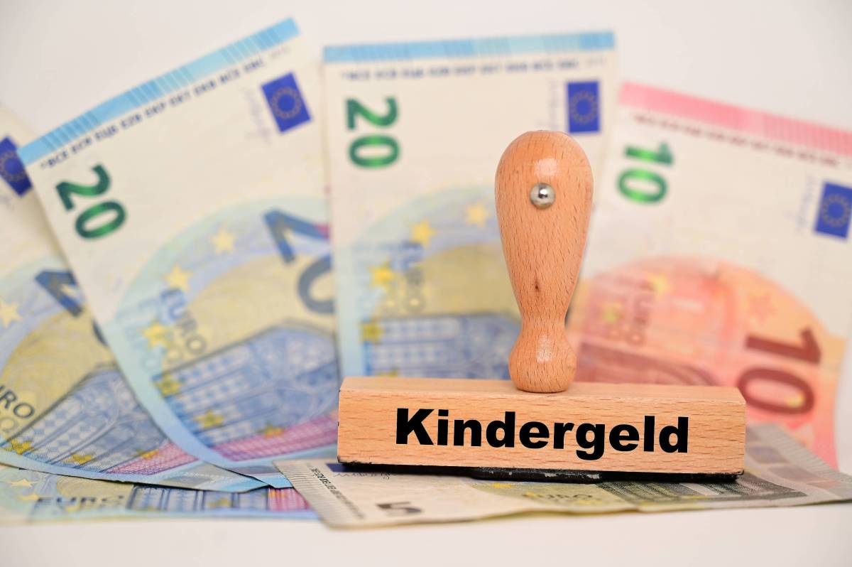 Auf einem Stempel steht das Wort "Kindergeld". Darunter liegen Geldscheine.