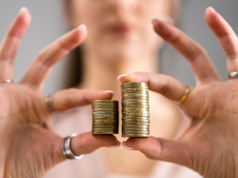 Eine Frau hält zwei Stapel Münzen in der Hand. Der linke ist kleiner als der rechte.