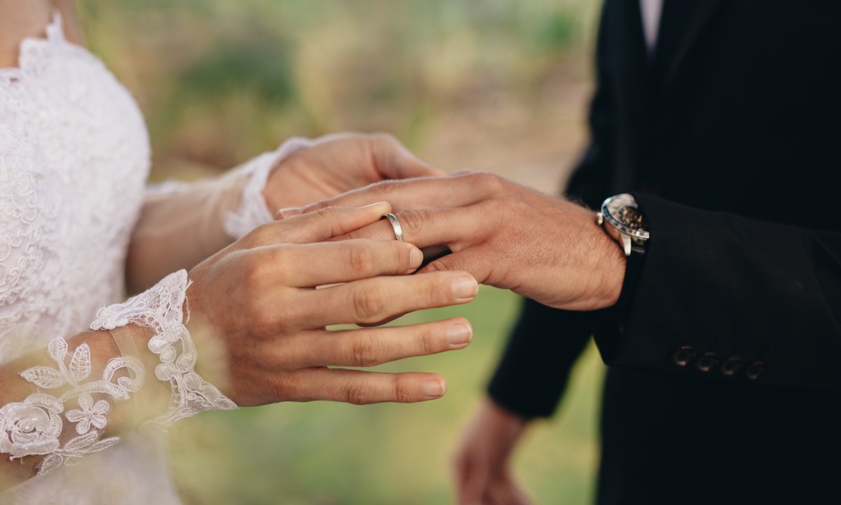 Eine Braut steckt dem Bräutigam den Ring an den Finger.