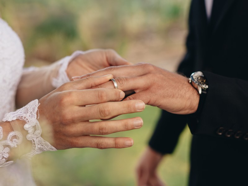 Eine Braut steckt dem Bräutigam den Ring an den Finger.