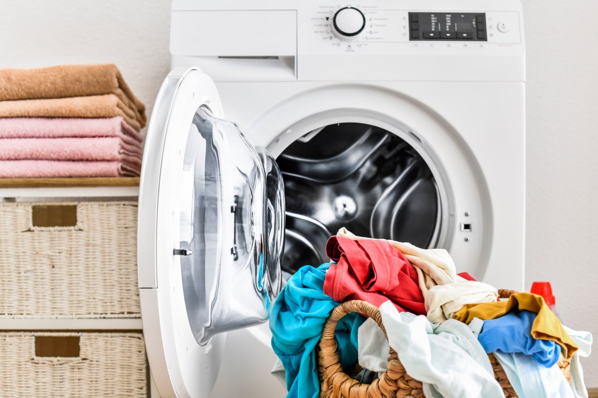 Ein voller Wäschekorb steht vor einer Waschmaschine.