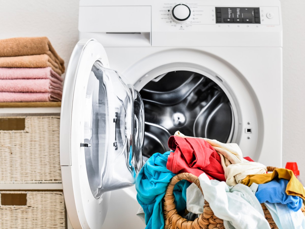 Ein voller Wäschekorb steht vor einer Waschmaschine.