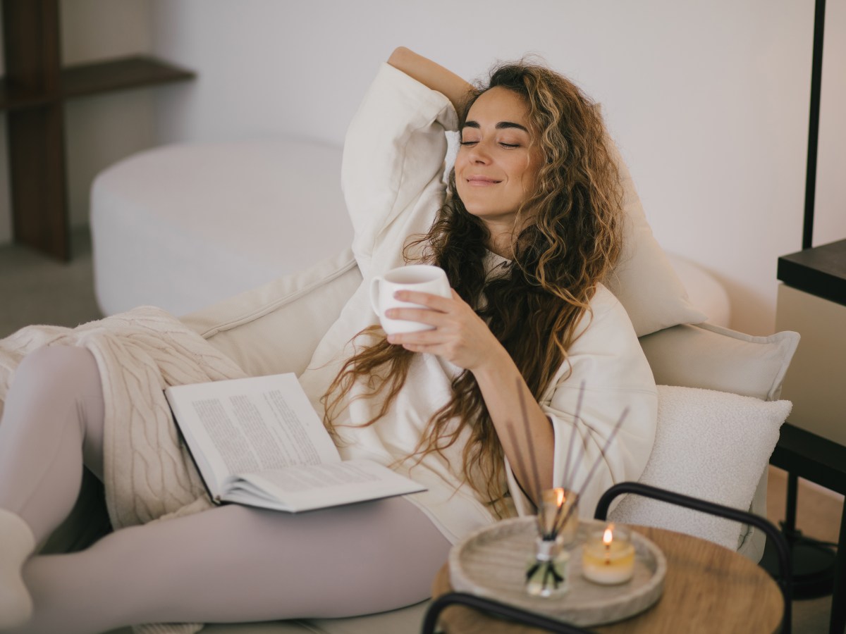 Frau liegt mit einer Decke und einem Buch auf dem Sofa