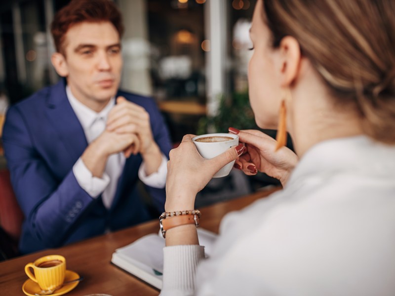 Kaffeetassen-Test: Geschäftsmann, der mit einer Frau ein Gespräch führt. Sie trinkt einen Kaffee.
