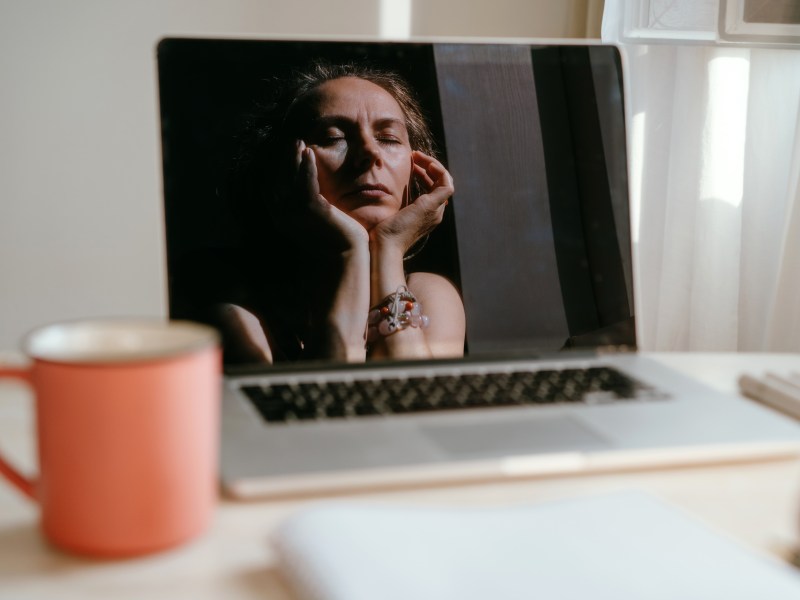 Porträt einer Frau, die am Schreibtisch sitz. Hier Spiegelbild spiegelt sich in ihrem Laptop.