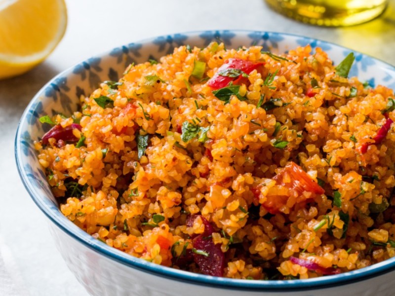 Eine Schüssel mit türkischem Bulgursalat. Daneben liegt eine Zitronenspalte.
