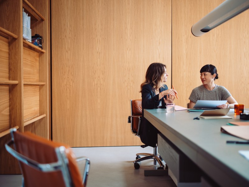 Zwei Frauen führen ein Gespräch an einem Bürotisch.