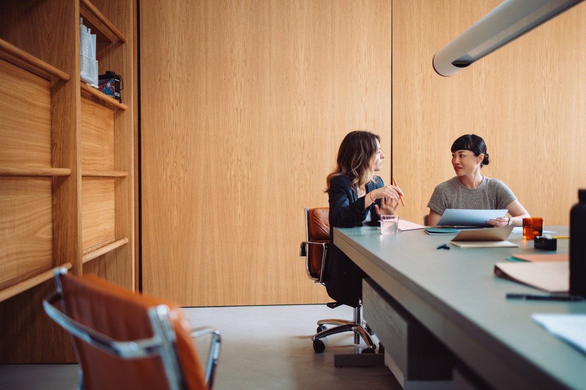 Zwei Frauen führen ein Gespräch an einem Bürotisch.