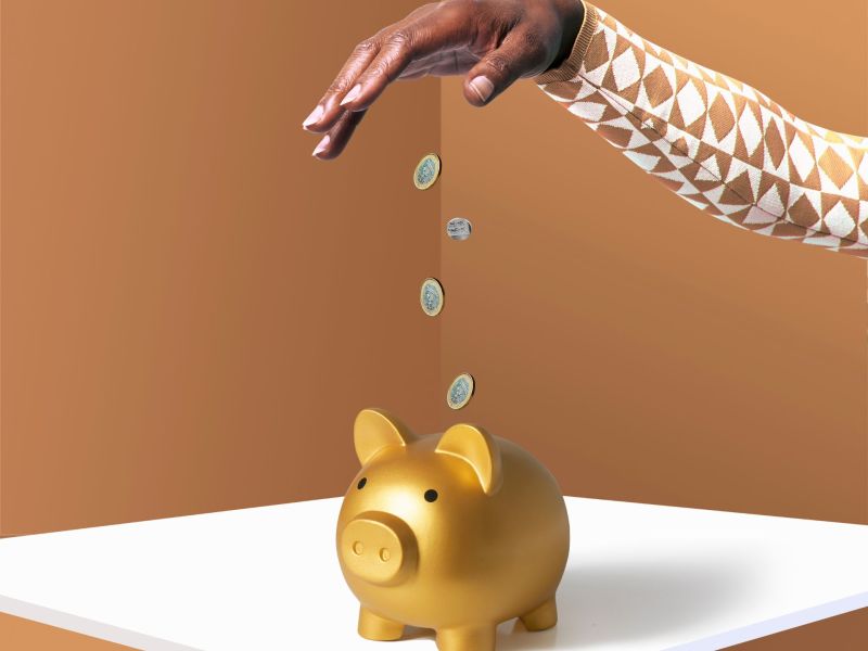 Eine Hand wirft Münzen in ein goldenes Sparschwein.