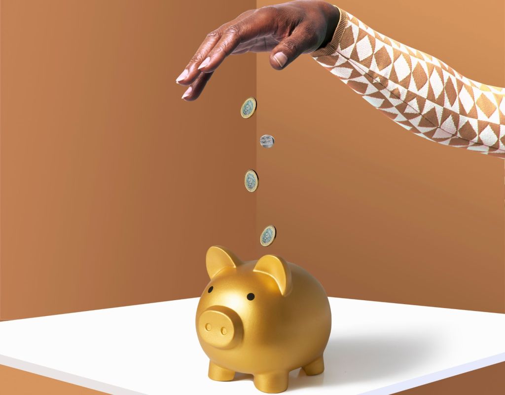 Eine Hand wirft Münzen in ein goldenes Sparschwein.