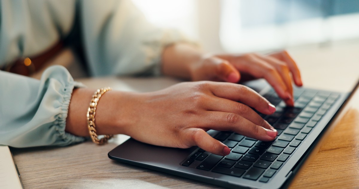Eine Frau mit roten Fingernägeln tippt auf einer Tastatur.