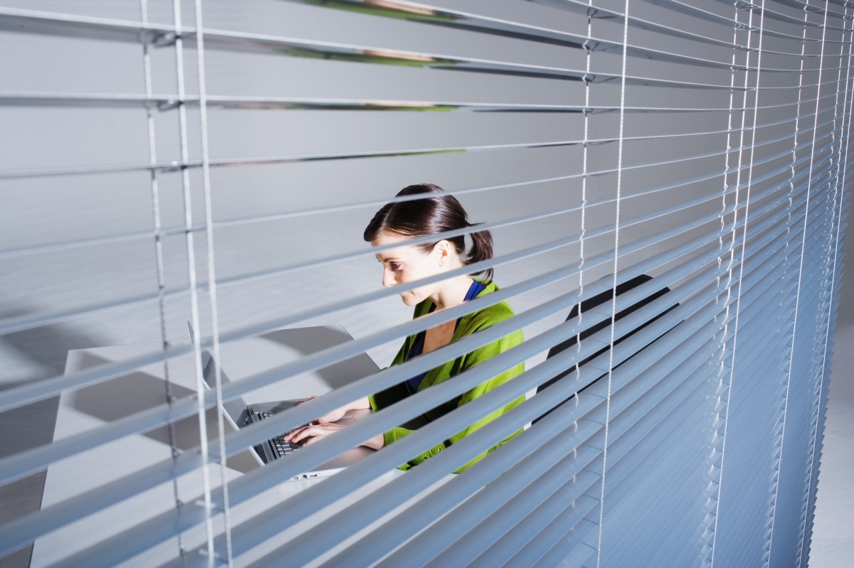 Junge Frau mit Laptop, Blick durch Fensterrollo.