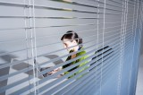 Junge Frau mit Laptop, Blick durch Fensterrollo.