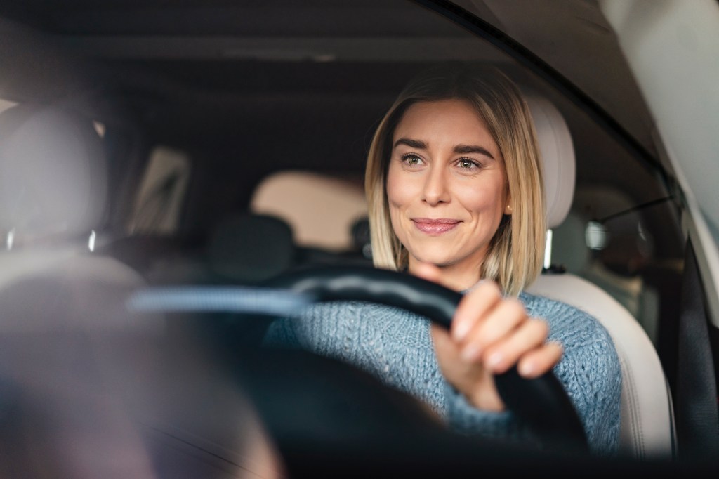 Porträt einer lächelnden jungen Frau am Steuer eines Autos