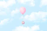 Ein einzelnes rosa Sparschwein, das an einem Ballon mit einem Seil befestigt ist, das durch die Wolken schwebt.