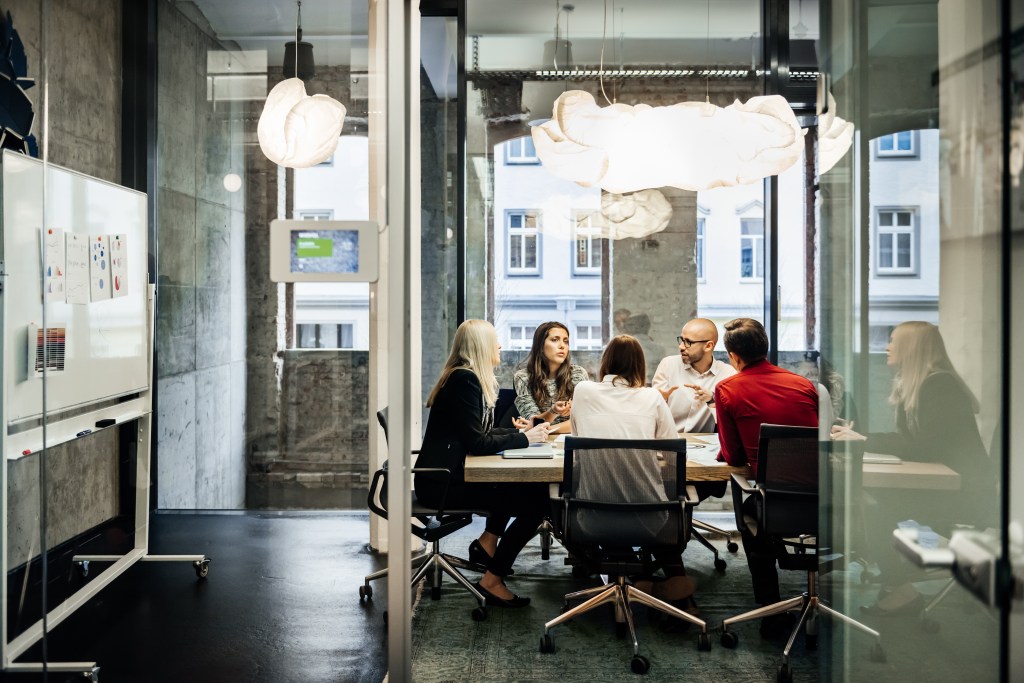 Eine Gruppe von Personen sitzt während eines Meetings in einem hellen, modernen Büro an einem Tisch.