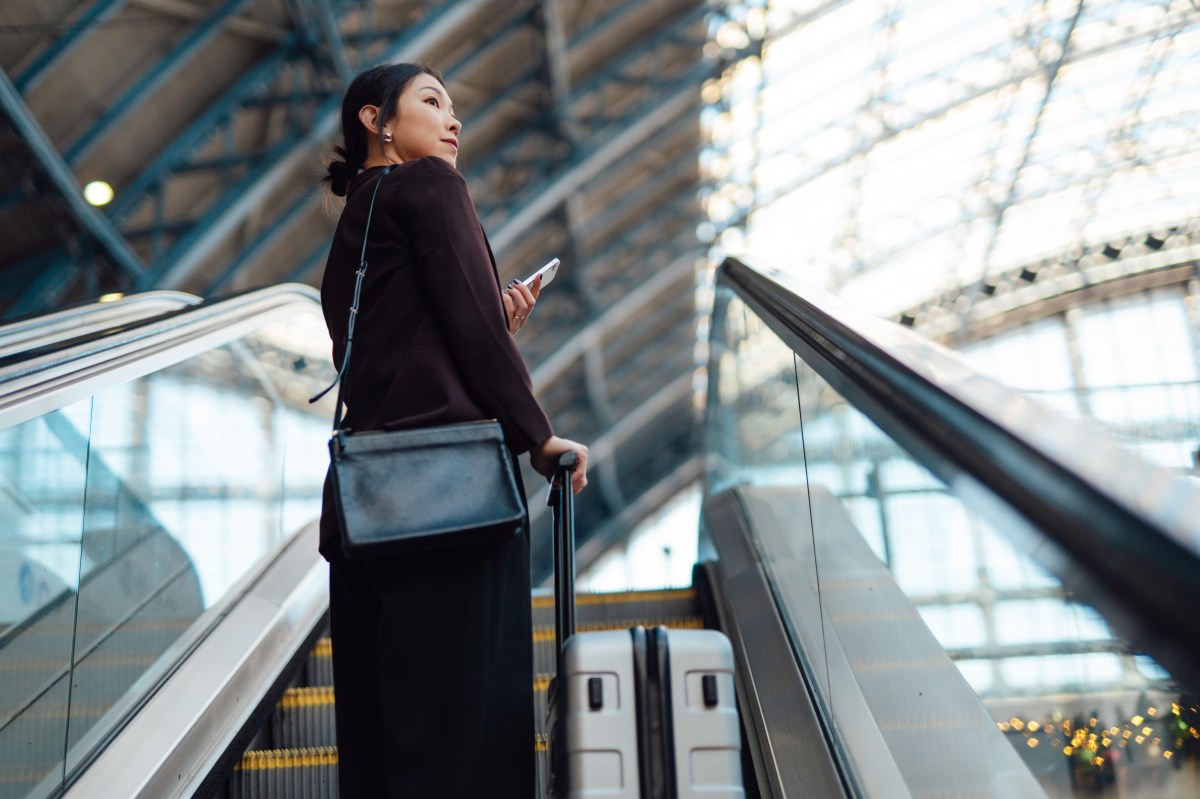 Junge asiatische Geschäftsfrau mit Smartphone, trägt Gepäck am Flughafen, unterwegs auf Geschäftsreise.