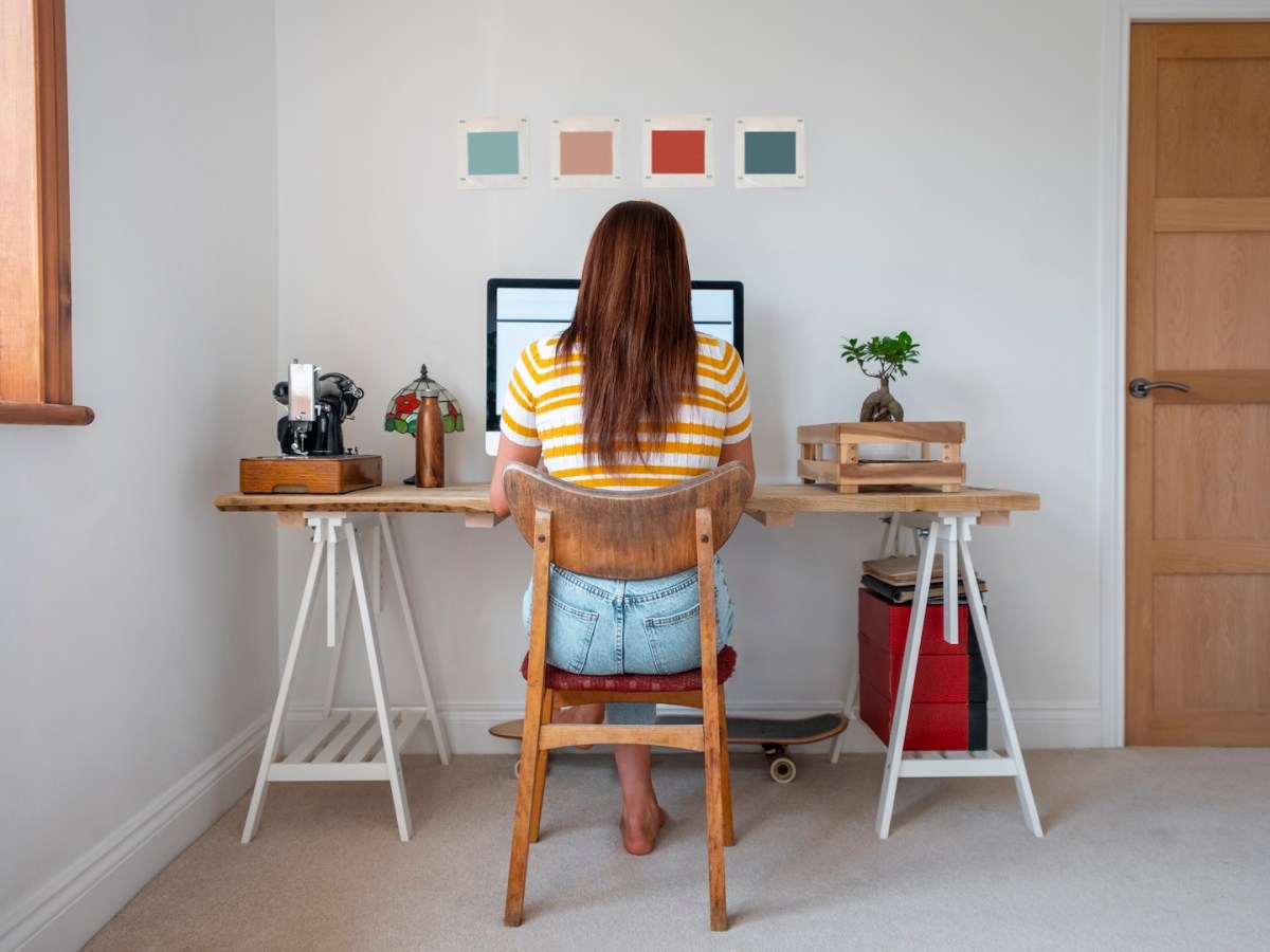 Eine Junge Frau, die im Homeoffice an ihrem Schreibtisch sitzt und arbeitet.