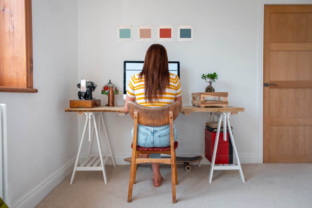 Eine Junge Frau, die im Homeoffice an ihrem Schreibtisch sitzt und arbeitet.