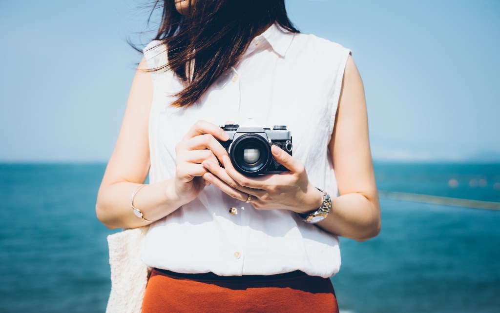 Mädchen fotografiert mit Vintage-Filmkamera am Strand an einem sonnigen Tag