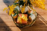 Mimosenblüten in der Vase, kleine Keramikdekor und ein Geschenk auf einem Tablett auf dem Holztisch.