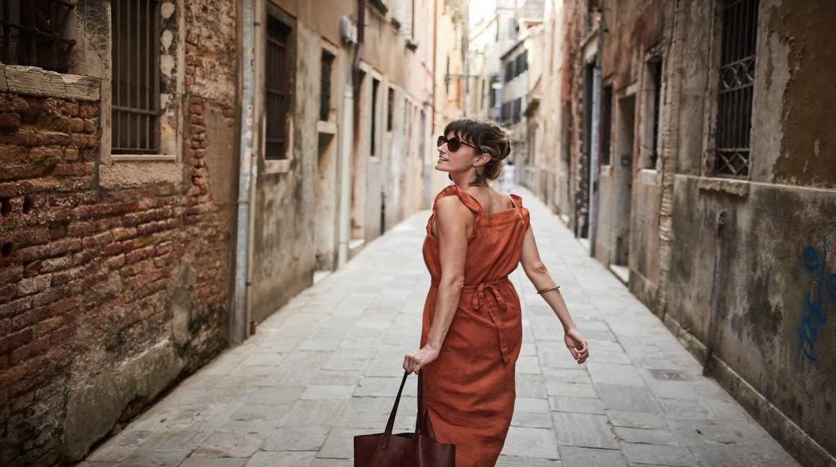 Eine Frau mit Sonnenbrille geht durch die Gassen einer italienischen Stadt.