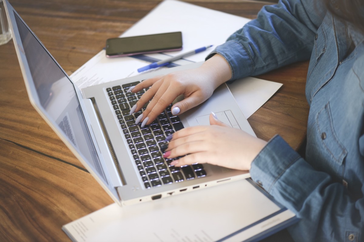 Eine Frau mit bunten Fingernägeln bearbeitet ihre Steuererklärung ab Laptop.