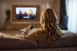 Eine Frau sitzt auf dem Sofa und schaut TV.