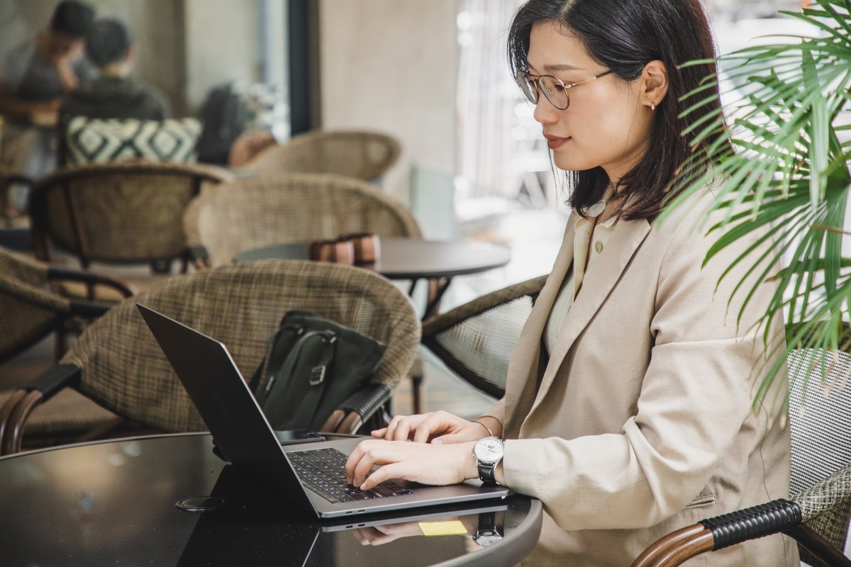 Eine asiatische Frau sitzt in einem Café und bearbeitet ihre Bewerbung am Laptop.l
