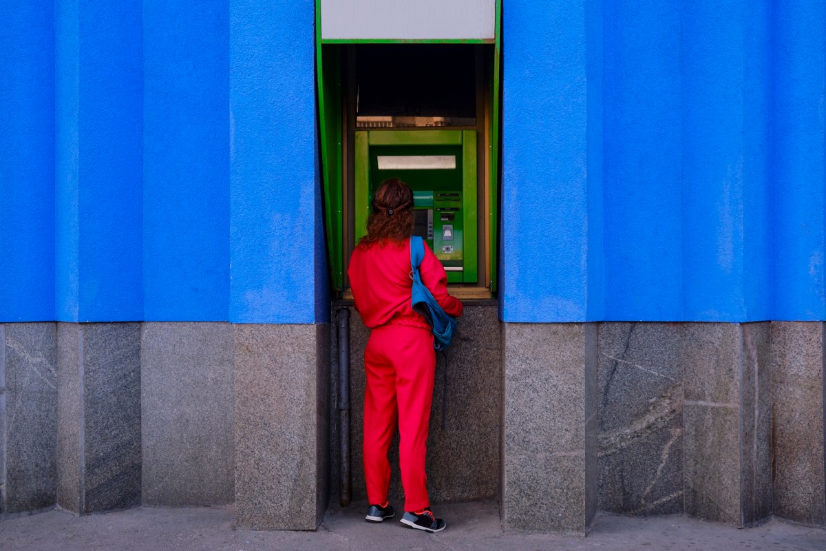 Frau in einem roten Bürooutfit hebt Geld an einem Automaten ab.
