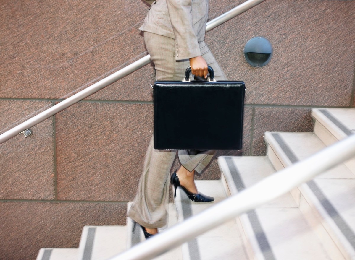 Eine Frau mit einer schwarzen Aktentasche läuft eine Treppe hoch.