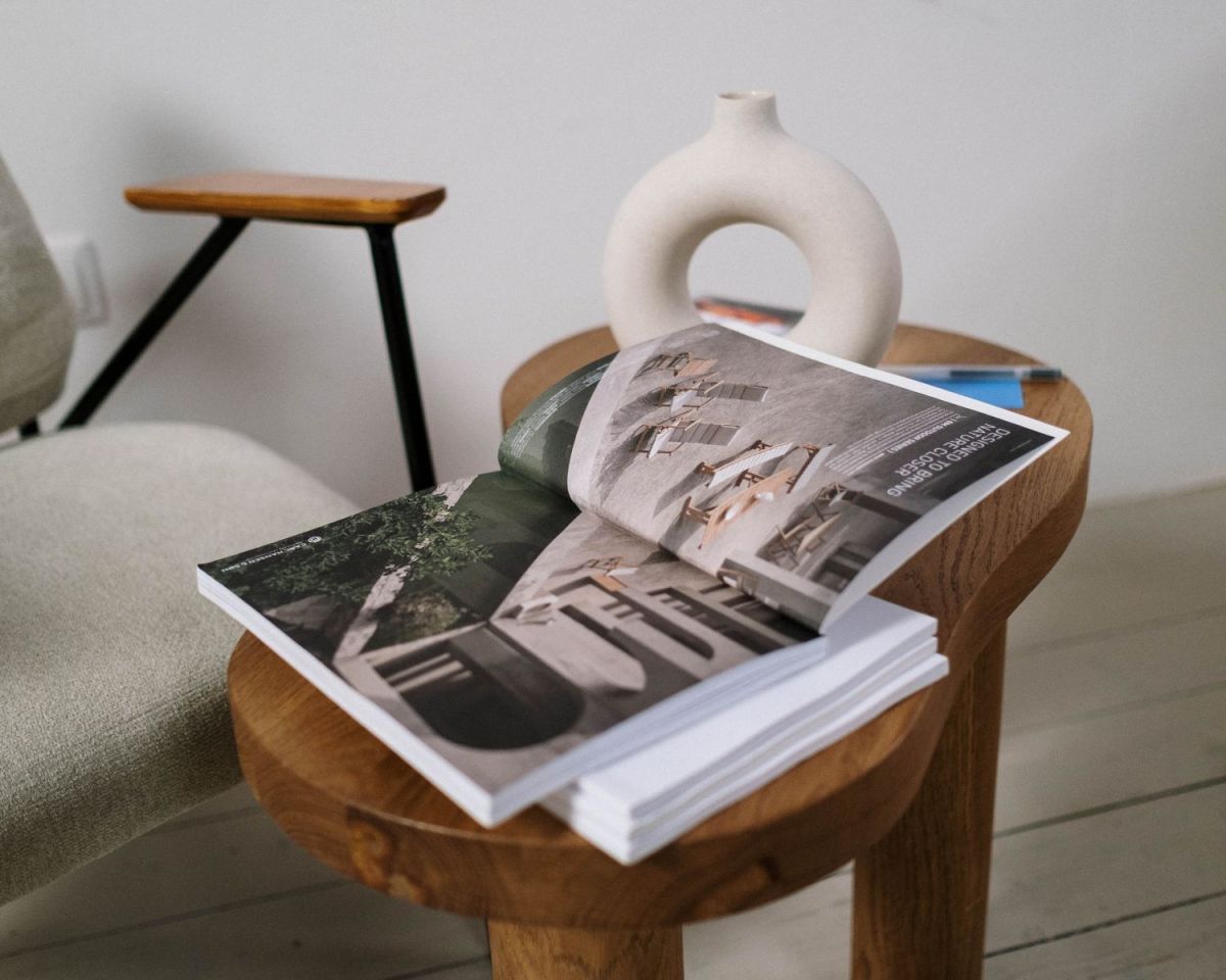Ein geöffnetes Buch auf einem Holztisch neben einer Vase und einem Stuhl.