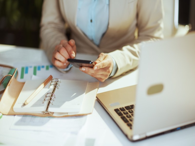 Frau im hellen Businessanzug im grünen Büro mit Laptop und Taschenrechner.