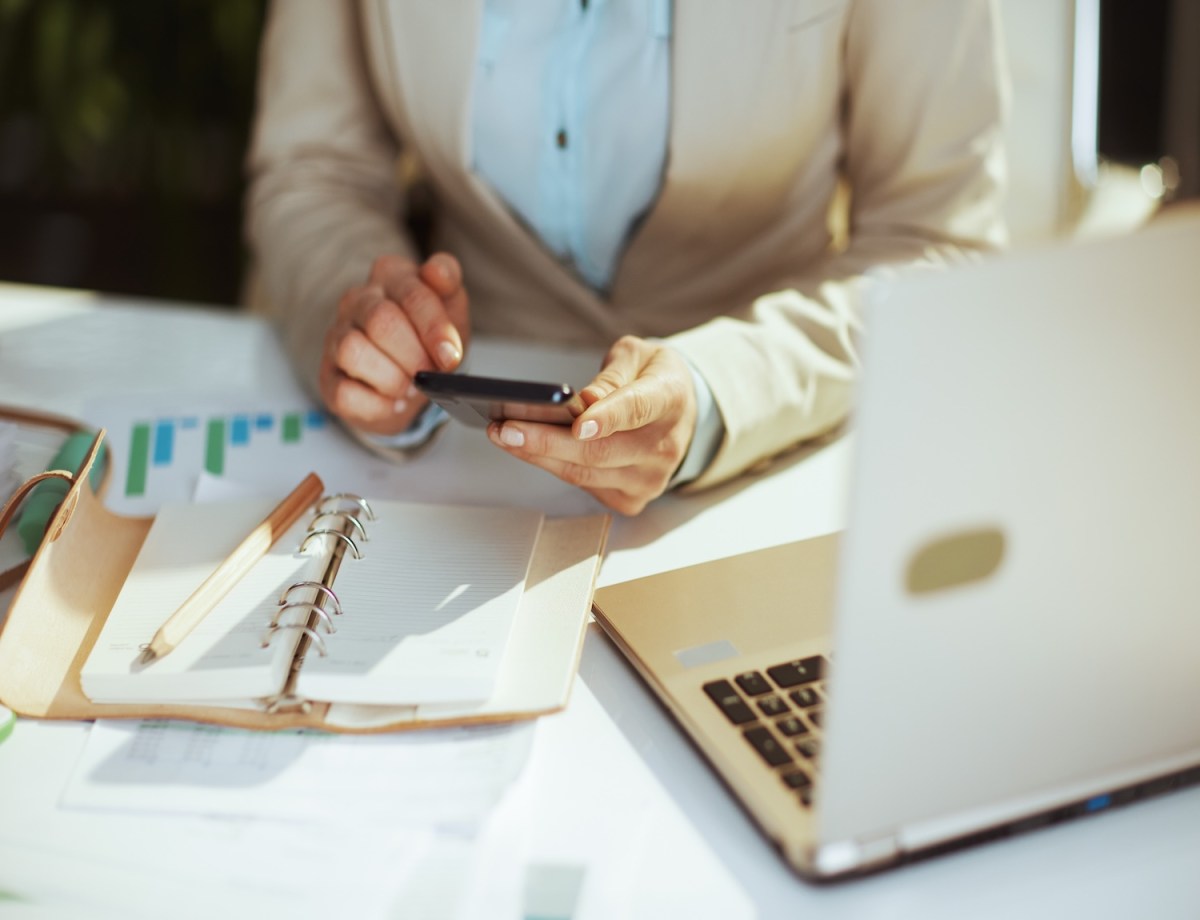 Frau im hellen Businessanzug im grünen Büro mit Laptop und Taschenrechner.