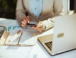 Frau im hellen Businessanzug im grünen Büro mit Laptop und Taschenrechner.