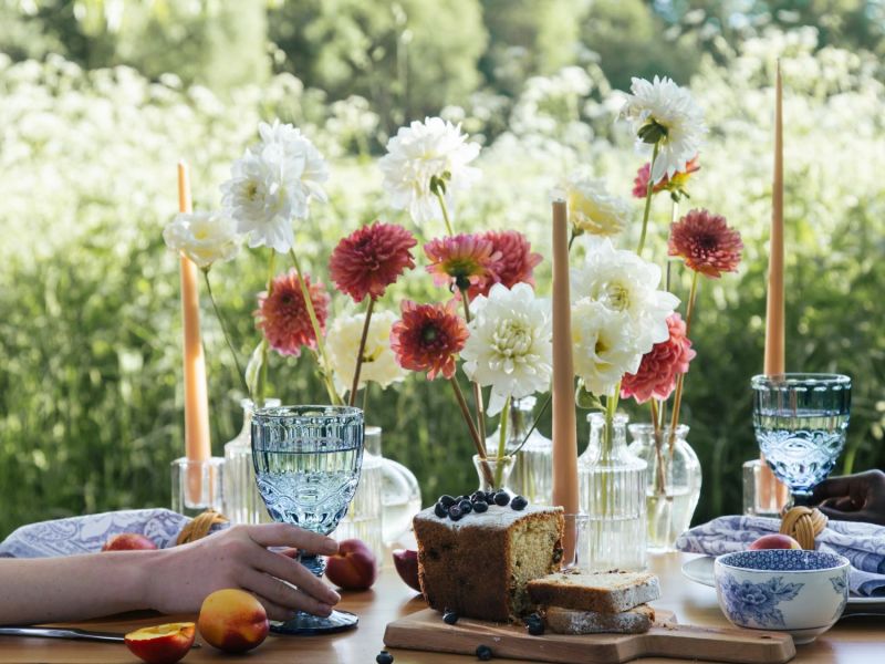 Tischdeko für eine Gartenparty mit Blumen, Kerzen und Geschirr