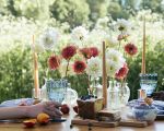 Tischdeko für eine Gartenparty mit Blumen, Kerzen und Geschirr