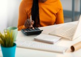 Junge Afroamerikanerin, die mit Laptop und Taschenrechner am Schreibtisch arbeitet.