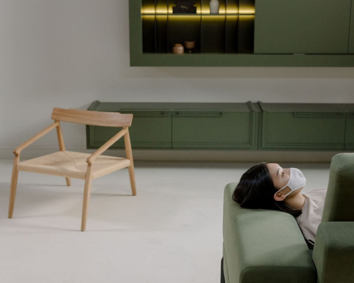 Frau liegt mit einer Maske vor dem Mund auf einem grünen Sofa